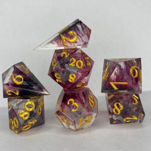 Könnte beinhalten: Satz von sechs transparenten Harz-Würfeln mit goldenen Zahlen und rosa, weißen und grauen Wirbeln. Die Würfel sind pyramidenförmig gestapelt.