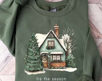 Może przedstawiać: Zielona bluza z zimową sceną domu z choinką i tekstem "tis the season".