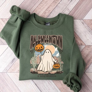 May include: Green sweatshirt with a retro-style graphic of a ghost holding a jack-o-lantern. The graphic says "Halloweentown Est. 1998" and "Where being original is vastly overrated."