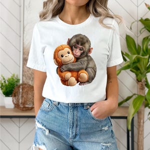 May include: White t-shirt featuring a graphic of two monkeys hugging. One monkey is brown and the other is orange. The t-shirt is made of a soft material and is suitable for casual wear.