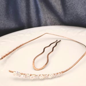 K&ouml;nnte beinhalten: Ein kupferfarbenes Metall-Haarband und eine passende gewellte Haarnadel. Das Haarband hat einen gebogenen Abschnitt, der mit kleinen, klaren, facettierten Kristallen verziert ist, die mit d&uuml;nnem Kupferdraht umwickelt sind. Die Haarnadel ist geh&auml;mmert.