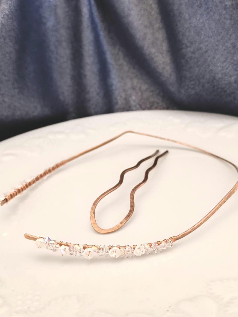 K&ouml;nnte beinhalten: Ein kupferfarbenes Metall-Haarband und eine passende gewellte Haarnadel. Das Haarband hat einen gebogenen Abschnitt, der mit kleinen, klaren, facettierten Kristallen verziert ist, die mit d&uuml;nnem Kupferdraht umwickelt sind. Die Haarnadel ist geh&auml;mmert.