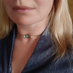 Peut inclure: Un collier ras de cou en or avec une pierre précieuse bleue et des accents de perles blanches.