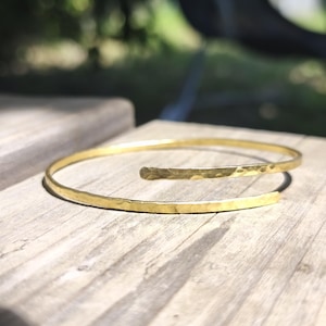 Peut inclure: Un bracelet jonc en métal doré au design ouvert. Le bracelet présente une finition martelée texturée sur toute sa surface, avec deux extrémités arrondies et légèrement effilées qui ne se rejoignent pas, formant une boucle ouverte ajustable.