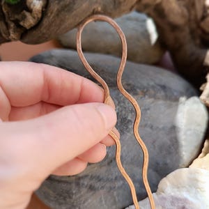 K&ouml;nnte beinhalten: Eine U-f&ouml;rmige Haargabel aus geh&auml;mmertem Kupfermetall. Das Accessoire verf&uuml;gt &uuml;ber eine abgerundete obere Schlaufe, die in zwei lange, gewellte Zinken &uuml;bergeht. Die Oberfl&auml;che des Kupfers weist durch das H&auml;mmern ein markantes, genopptes Finish auf.