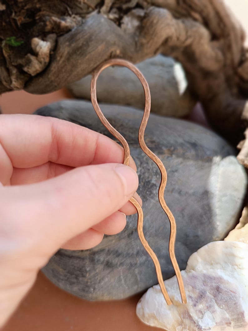 K&ouml;nnte beinhalten: Eine U-f&ouml;rmige Haargabel aus geh&auml;mmertem Kupfermetall. Das Accessoire verf&uuml;gt &uuml;ber eine abgerundete obere Schlaufe, die in zwei lange, gewellte Zinken &uuml;bergeht. Die Oberfl&auml;che des Kupfers weist durch das H&auml;mmern ein markantes, genopptes Finish auf.
