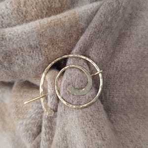 Peut inclure: Une épingle à châle en métal doré avec un motif en spirale. L'épingle est sur un tissu pelucheux brun et beige.
