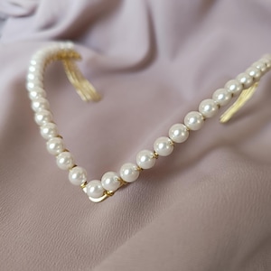 May include: A gold headband with a row of white pearls. The headband has two combs on the back for easy attachment to hair.