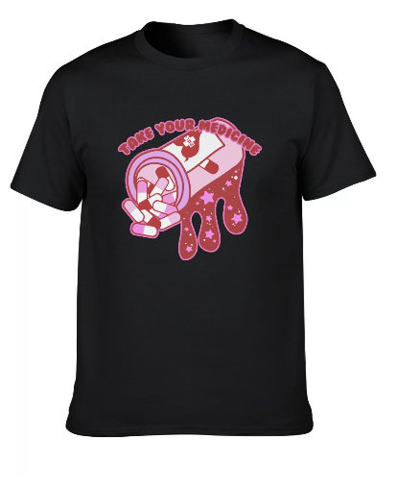 Peut inclure: T-shirt noir avec une illustration rose et blanche d'un flacon de m&eacute;dicaments et de pilules. Le texte "TAKE YOUR MEDICINE" est au-dessus du flacon. Le motif comprend des &eacute;toiles roses et un effet d&eacute;goulinant.