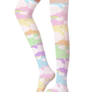 Op de afbeelding: Over-de-knie sokken met een pastel regenboog- en wolkenpatroon. De sokken hebben een herhalend ontwerp van wolken, regenbogen en sterren in tinten roze, blauw, geel en groen. De sokken zijn gemaakt van een zacht, rekbaar materiaal.