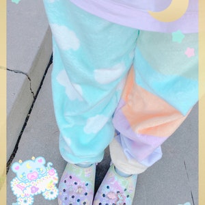 May include: Pastel-colored pajama pants with cloud and color block patterns. The pants are paired with matching pastel clogs adorned with charms. The image also features the text "KAWAII GOODS".