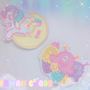 May include: Two embroidered iron-on patches. One features a white unicorn with a rainbow mane and tail, sleeping on a yellow crescent moon. The other features a pink creature with a single eye, holding a yellow ice cream cone and a purple flower. Both patches have a white background.