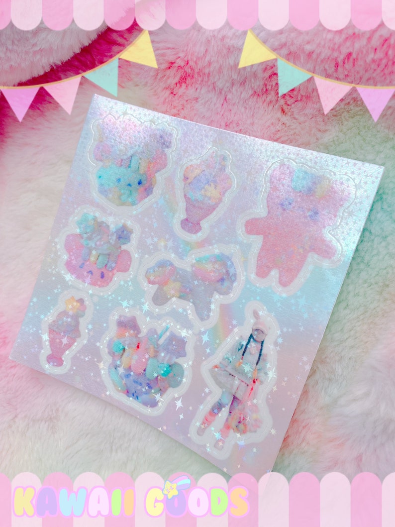 May include: A sheet of iridescent holographic stickers featuring a variety of cute pastel-colored designs, including a bear, ice cream cones, and a girl in a winter coat. The stickers are on a white background with silver glitter stars.