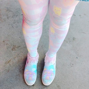 May include: A pair of pastel blue and pink patterned tights with a cartoon character design. The tights are worn with a pair of white canvas shoes with a cartoon character design.