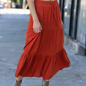 May include: A rust-colored tiered maxi skirt with a drawstring waist. The skirt is made of a soft, flowy fabric and has a relaxed fit.