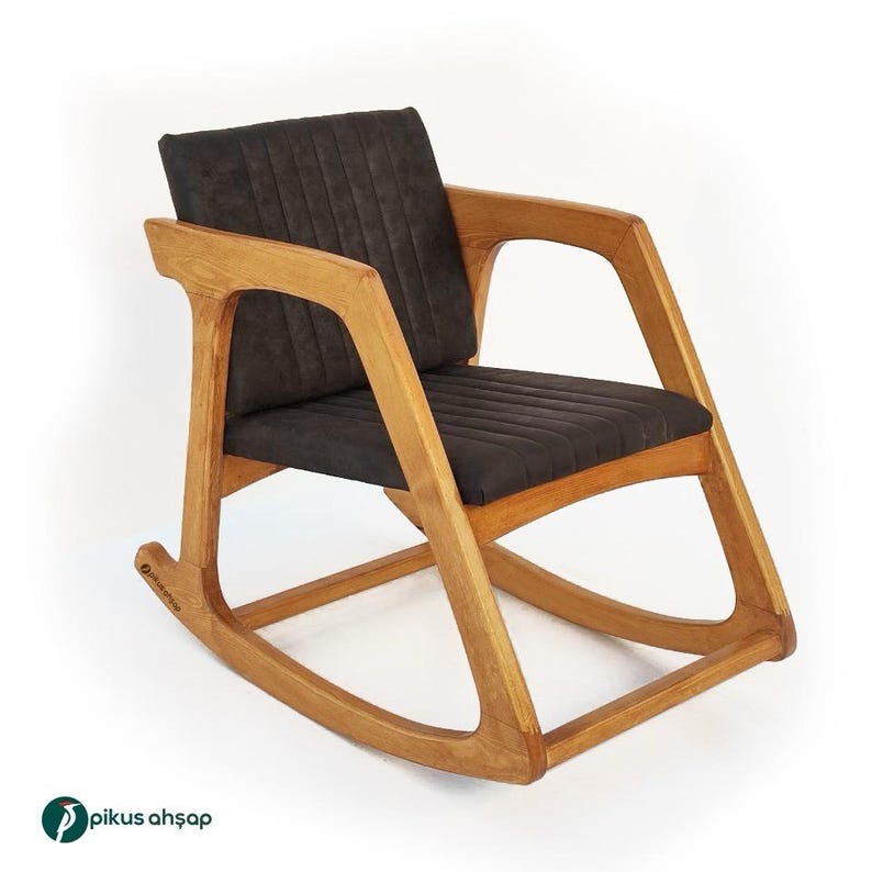 Peut inclure: Une chaise &agrave; bascule dot&eacute;e d'une structure en bois brun clair avec une finition grain naturel et un si&egrave;ge ainsi qu'un dossier rembourr&eacute;s gris fonc&eacute;. Les coussins pr&eacute;sentent des lignes cousues verticales et la marque Pikus Ahşap est visible.