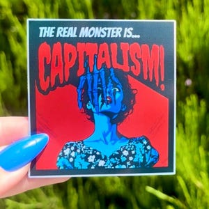 Puede incluir: Una pegatina con fondo rojo y negro que muestra a una mujer con una mano que le llega a la cara. El texto "THE REAL MONSTER IS... CAPITALISM!" est&aacute; impreso en blanco.