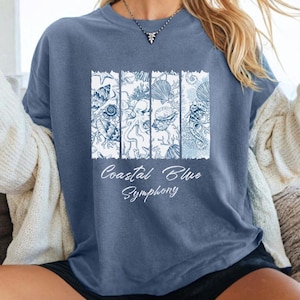 Könnte beinhalten: Blaues T-Shirt mit einem weißen und blauen Küstenmotiv. Das Design zeigt Illustrationen von Muscheln, Seepferdchen und anderen Meereslebewesen. Der Text "Coastal Blue Symphony" ist darunter gedruckt.