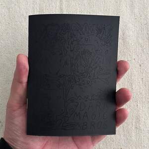 Puede incluir: Ilustraci&oacute;n en blanco y negro de un libro con un dise&ntilde;o fantasioso y espeluznante. La portada presenta una variedad de personajes y objetos, incluyendo fantasmas, murci&eacute;lagos y una calavera. El t&iacute;tulo del libro es "Dark Magic Bros."