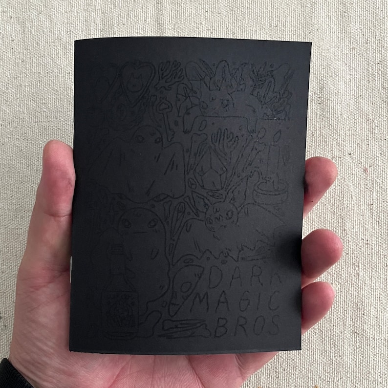 Puede incluir: Ilustraci&oacute;n en blanco y negro de un libro con un dise&ntilde;o fantasioso y espeluznante. La portada presenta una variedad de personajes y objetos, incluyendo fantasmas, murci&eacute;lagos y una calavera. El t&iacute;tulo del libro es "Dark Magic Bros."