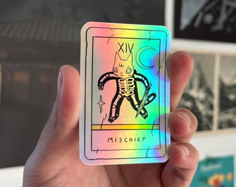 May include: A holographic tarot card with a black and white illustration of a skeleton cat holding a knife. The card is labeled "XIV" and "MISCHIEF".