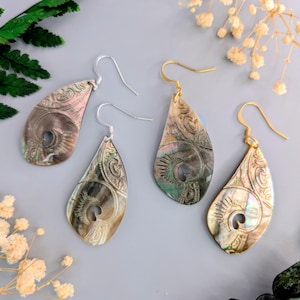 Peut inclure: Quatre paires de boucles d'oreilles en forme de goutte d'eau avec des motifs sculptés complexes. Deux paires ont des crochets argentés et deux ont des crochets dorés. Les boucles d'oreilles sont iridescentes avec des nuances de rose, de vert et de brun.