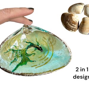 Puede incluir: Un plato de concha de mar con un pez verde y negro pintado en su interior. La concha es de color azul claro y tiene un borde dorado. El texto "2 in 1 design" es visible debajo de la concha.