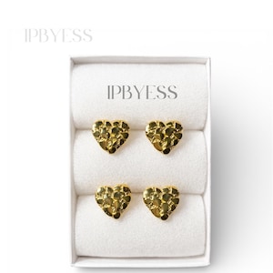 May include: Four gold-colored heart-shaped stud earrings in a white box. The earrings have a textured surface. The box is lined with white fabric. The brand name "IPBYESS" is printed on the box.