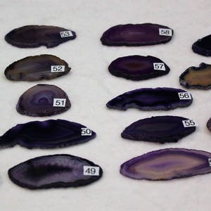 May include: Assortment of 16 purple agate slices, each with unique banding patterns and numbered 44 through 61.
