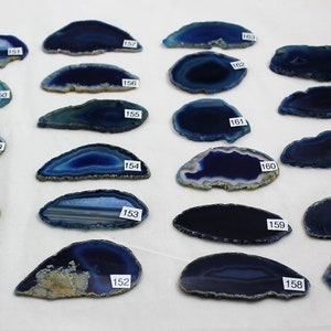 May include: Twenty blue agate slices with white and brown banding. The agate slices are arranged in rows on a white surface.