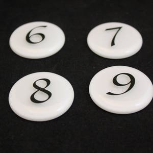 Puede incluir: Cuatro azulejos de cer&aacute;mica redondos blancos con los n&uacute;meros negros 6, 7, 8 y 9 impresos en ellos.