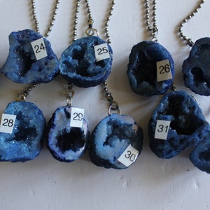 May include: Twelve blue crystal geodes on silver chains with numbered tags. The geodes are all different shapes and sizes, and they have a sparkly, iridescent finish.