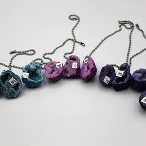 May include: Eight crystal geodes on silver chains, each with a number label. The geodes are in shades of blue, purple, and pink.