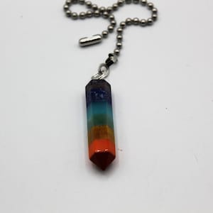 May include: A multi-colored crystal pendant with a silver chain. The crystal is a layered, pointed, prism shape with seven colors: purple, blue, green, yellow, orange, red, and brown.