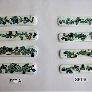 May include: Two sets of three rectangular glass tiles with a white background and a design of blue, green, and gold abstract shapes. The tiles are labeled "SET A" and "SET B".