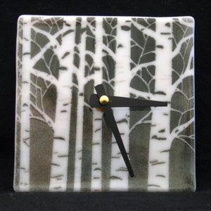 May include: A square glass clock with a white birch tree design. The clock face is white with black hands and a gold center.