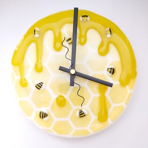 May include: A yellow and white clock with a honeycomb pattern and dripping honey. The clock has black hands and bee accents.