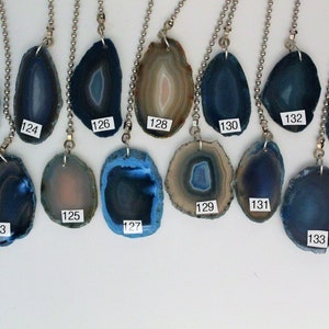 May include: Fifteen agate pendant charms with silver chains. The agates are various shades of blue and brown with white banding. The charms are numbered 121 through 135.