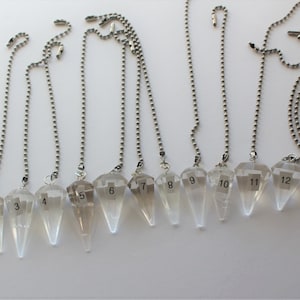 May include: Thirteen clear quartz crystal pendulums with silver chains, numbered 1 through 13.