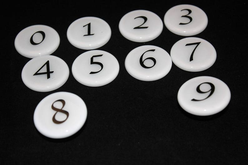 Puede incluir: Nueve fichas redondas blancas con n&uacute;meros negros del 0 al 9.