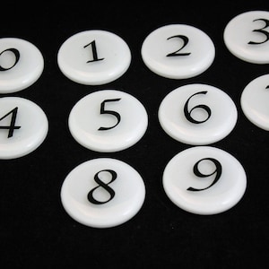 May include: Ten white round discs with black numbers 0 through 9 on them.
