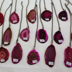 May include: Assortment of 18 pink agate slices with silver chains. Each slice is unique with different patterns and shades of pink. The slices are numbered 110 through 128.