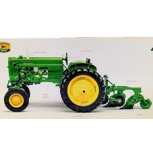 May include: A green John Deere model 40 tractor toy with yellow wheels and a rear plow attachment. The packaging features the John Deere Collectors Edition logo, the number 4, and labels pointing to features like authentic graphics and working steering.