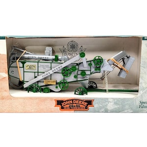 May include: A 1/28th scale John Deere 1938 thresher model in a display box. The machine is silver with green wheels, gears, and accents. It features the John Deere logo, text, and a small ladder. The packaging is labeled Special Edition.