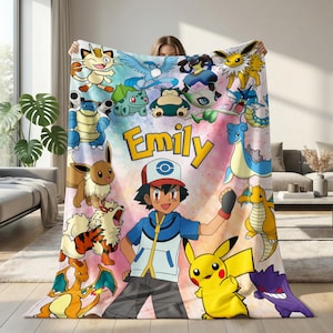 May include: A soft fleece blanket featuring a colorful collage of various Pokémon characters surrounding a central illustration of Ash Ketchum. The name Emily is printed in large yellow letters above the character. The background has a watercolor effect.