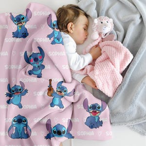 K&ouml;nnte beinhalten: Eine hellrosa Fleecedecke mit einem sich wiederholenden Muster der blauen Figur Stitch in verschiedenen Posen, durchsetzt mit dem Namen Sophia in wei&szlig;em Text und kleinen wei&szlig;en Herzumrissen. Die Decke hat eine weiche Textur.