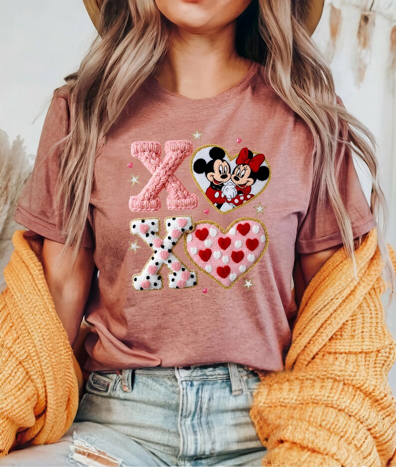 May include: Dusty rose t-shirt featuring an embroidered design with the letters "XO", a heart with Mickey and Minnie Mouse, and a heart filled with red hearts. The design includes white polka dots and star accents.