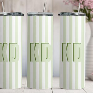May include: Three tall, cylindrical stainless steel tumblers with lids and metal straws. Each tumbler features a vertical striped pattern in alternating shades of light green and white, with the bold, dark green capital letters KD centered.