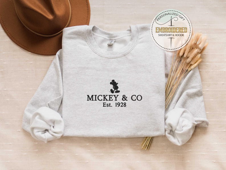 Puede incluir: Una sudadera gris con una silueta negra de Mickey Mouse y el texto "Mickey & Co. Est. 1928".