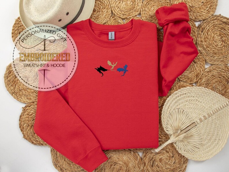 May include: A red embroidered sweatshirt with three dragon silhouettes in black, gold, and blue. The text "PERSONALIZED GIFT EMBROIDERED SWEATSHIRT & HOODIE" is in a circle on the left. A straw hat and fan are in the background.